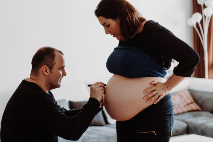 Olivier écrit le prénom de leur première fille sur le ventre de Florence à l'aide d'un rouge à lèvres. Ils profitent de la séance photos grossesse pour immortaliser le choix du prénom de leur premier enfant.